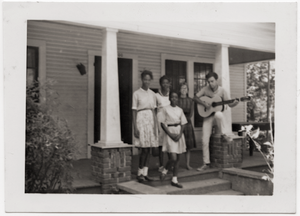 White civil rights worker playing guitar on the front steps of the Freedom House (Kathy Dahl, 2d from right)