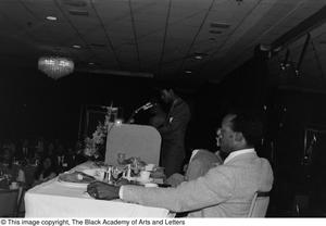 Photograph of an unidentified man standing close to a podium