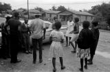 Roosevelt Barnett, Richard Boone, Lula Williams, and others, standing in the dirt lot in front of Pugh's Superette on Foster Street in Newtown, a neighborhood in Montgomery, Alabama.