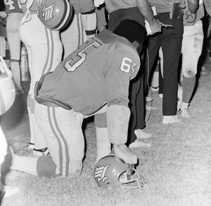 Football player kneeling with a helmet