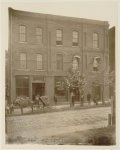 [African Americans standing outside brick building "Frien[dship] Phar[macy]" and "Post Office", with horse-drawn carriage in street]