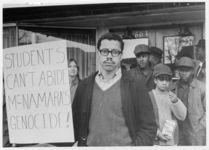 Mississippi State Sovereignty Commission photograph of an unidentified African American man holding a protest sign reading "Students can't abide McNamara's genocide!" along with other demonstrators during an Anti-Vietnam War demonstration protesting Secretary of Defense Robert McNamara's visit to Jackson, Mississippi, 1967 February 24