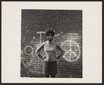 [African American woman standing in front of wall with peace sign, Lower West Side, Buffalo]