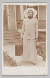 Photographic postcard of unidentified woman holding a travel bag