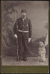 [Civil War veteran holding bayoneted rifle and dog holding flag in front of painted backdrop]