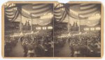 [Interior view of a large convention hall filled with people sitting in chairs]