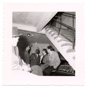 Flip Phillips (second from left), Norman Granz (second from right), and other men,talking under staircase, undated.] [Black-and- white photoprint