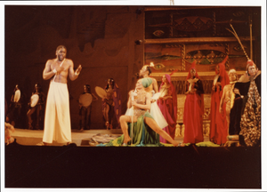 Performance picture of Eartha Kitt (sitting, green turban, center stage), a man in white standing to the left, and many cast members]. [color photoprint