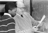 An Educational Opportunity Program student and a professor review an equation in front of a blackboard, 1984