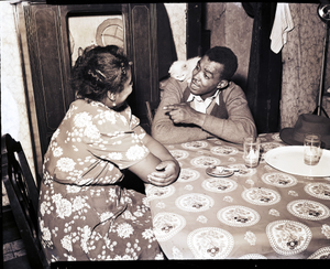 Couple talking at kitchen table with cat on man's shoulder : black-and-white photonegative