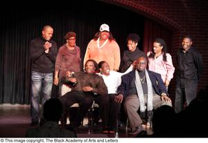 Performer, man, and Curtis King sitting on stage with three women and three men standing