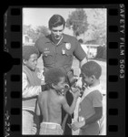 Three African American children mingling with police officer at Nickerson Gardens Housing Project in Los Angeles, Calif., 1985