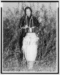 [Zora Hurston, full-length portrait, standing, facing front, beating tall drum]