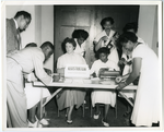 Men and women filling out registration cards at table with 'Registration courtesy of San Diego City and County Convention Bureau' sign