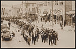 [Parade of Civil War veterans and children carrying American and Alaska flags on urban downtown street]