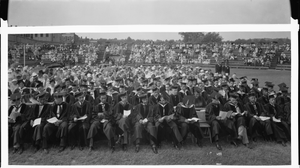 Seated group of graduates in academic robes with spectators seated behind and in bleachers, Howard University : cellulose acetate photonegative, banquet camera format