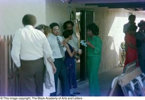 Photograph of a fenced area near a garage where groups of people are standing around