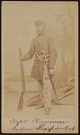 [Captain William Plumer (Plummer) of the 1st Massachusetts Sharpshooters Company in uniform with target rifle, revolver and sword, standing in front of painted backdrop showing trees]