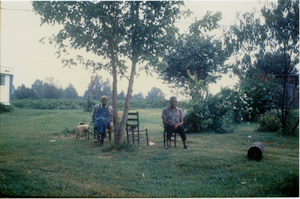 Charlie Hill and unidentified man (r. to l.), seated on a lawn