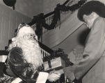 George Wallace dressed up as Santa Claus, handing a gift to an African American man at the Governor's Mansion.