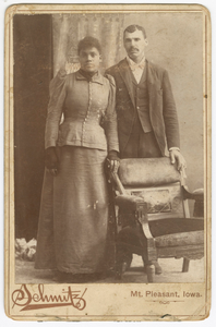 Photograph of a couple standing behind a chair