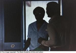 Photograph of two shadowed men standing near a doorway