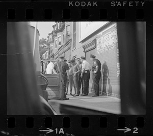 Police standing outside of a patrol car and speaking with a group of young Black men on the sidewalk, most likely after unrest broke out during student demonstrations