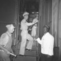 Man in military uniform boarding a train while African American railroad employee stands by, ca. 1950's