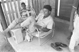 Man sitting on a lawn chair on the front porch of a brick house in Newtown, a neighborhood in Montgomery, Alabama.