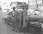 Two African-American men standing on the sidewalk in front of a car, Seattle, ca. 1950's