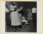 [African American women clapping and singing as a little girl seated follows along during a service at a store front church in Buffalo, New York]