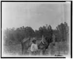 [African American boy standing with horse attached to plow]