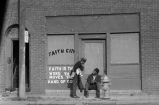 Two men talking in front of "Faith City" building.