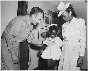 "Brig. Gen. Robert N. Young, Commanding General of the Military District of Washington, assists Melba Rose, aged 2, daughter of Mrs. Rosie L. Madison,...in viewing the Silver Star posthumously awarded her father 1st Lt. John W. Madison, of the 92nd Infantry Division, who was killed in action in Italy..."