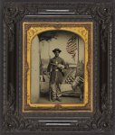 [Unidentified African American soldier in Union uniform with a Austrian Lorenz rifle-musket and Remington revolver in front of painted backdrop showing weapons and American flag at Benton Barracks, Saint Louis, Missouri]