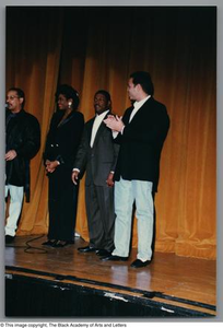 Low angle shot from the corner of a stage, focusing on three men and a woman standing on the stage