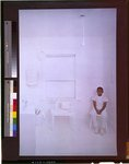 [African American boy, dressed in white, sitting in a poorly furnished room in which everything has been coated in white paint]