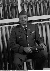 Col. Joe D. Sasser posing in front of drill rifles