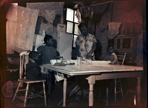 Woman ironing on kitchen table while three small children watch: black-and-white photonegative