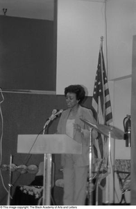 Woman standing at podium and addressing guests at conference