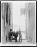 [Three African American men lifting a piece of equipment, with block and tackle, at the Standard Engraving Company, Washington, D.C.(?)]