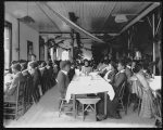 [Interior view of dining hall, decorated for the holidays, with students sitting at tables at the Tuskegee Institute]