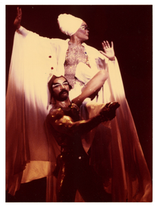 Performance picture of Eartha Kitt (in a white turban), a man is in front of her]. [color photoprint