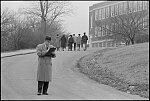 [F. Brent Sandidge, General Supervisor of Instruction for Warren and Rappahannock counties looking at book, as African American students walk up the driveway, outside Warren County High School, Front Royal, Virginia]