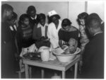 [Woman washing baby doll in class of the National Youth Administration and Civilian Conservation Corps, with nurse and nine other black men and women watching]