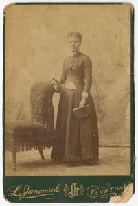 Photograph of a woman standing next to a chair and holding a book