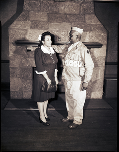 Uniformed soldier and woman standing in front of fireplace : photonegative.