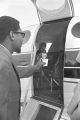 Richard Boone holding a paper cup outside the open door of a plane at the airport in Montgomery, Alabama.