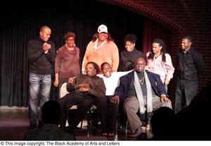 Performer, man, and Curtis King sitting on stage with three women and three men standing