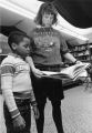 A female education student looks over a book with a young boy in the Hartman Education Clinic, 1988